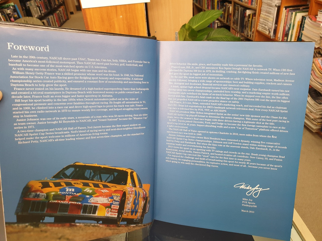 NASCAR history book foreword spread with orange race car photo and white script signature