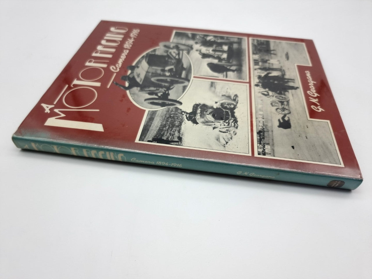 Hardcover book with maroon cover featuring vintage race-car photo collage, angled view