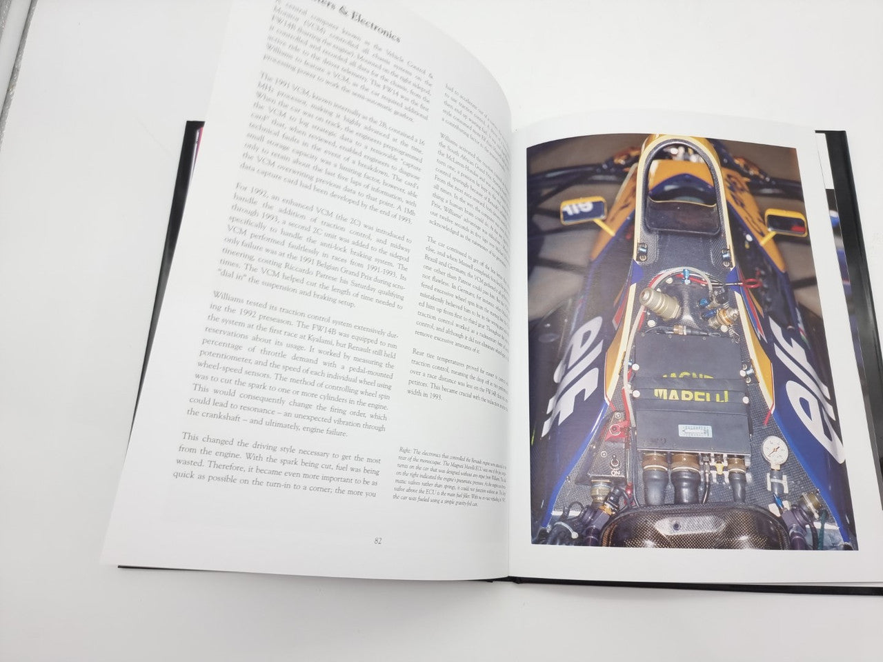 Open photo book showing dense text and a close-up of a race cockpit on right page