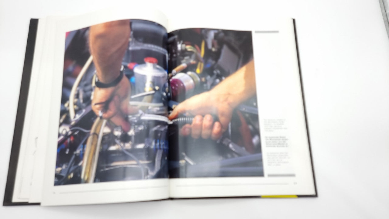 Photographic review book page showing hands working on a race car engine.