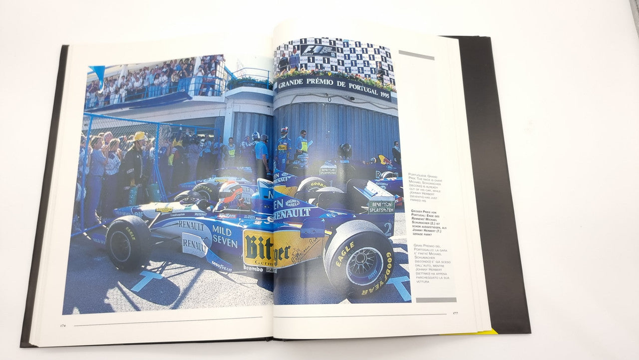 Photographic review book open to a color spread featuring a blue Formula 1 car on track