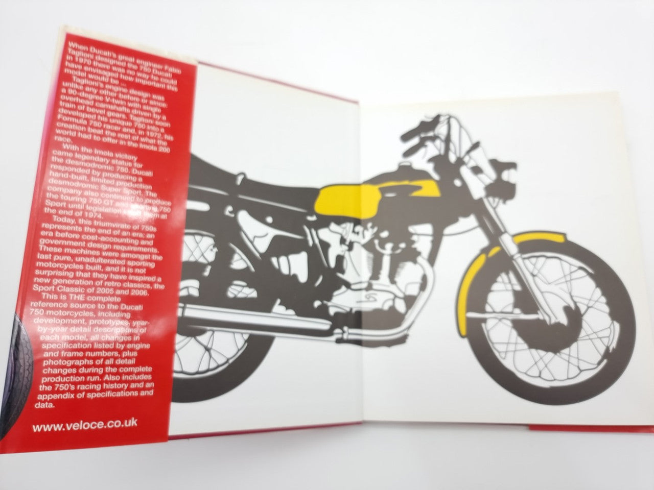 Open motorcycle history book showing a red text page and black bike silhouette
