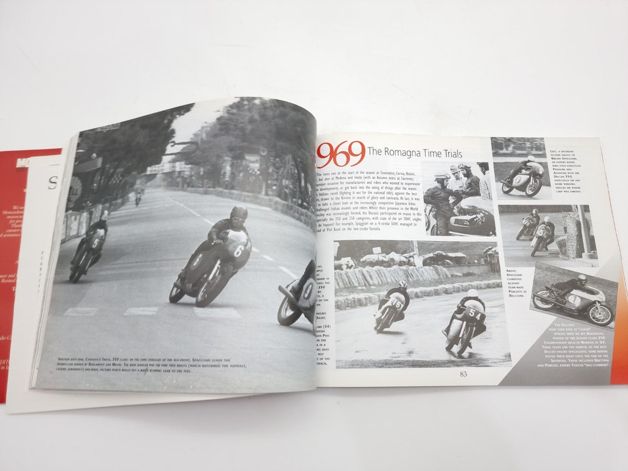 Open motorcycle history book spread with race scene photo and motorcycle action shots