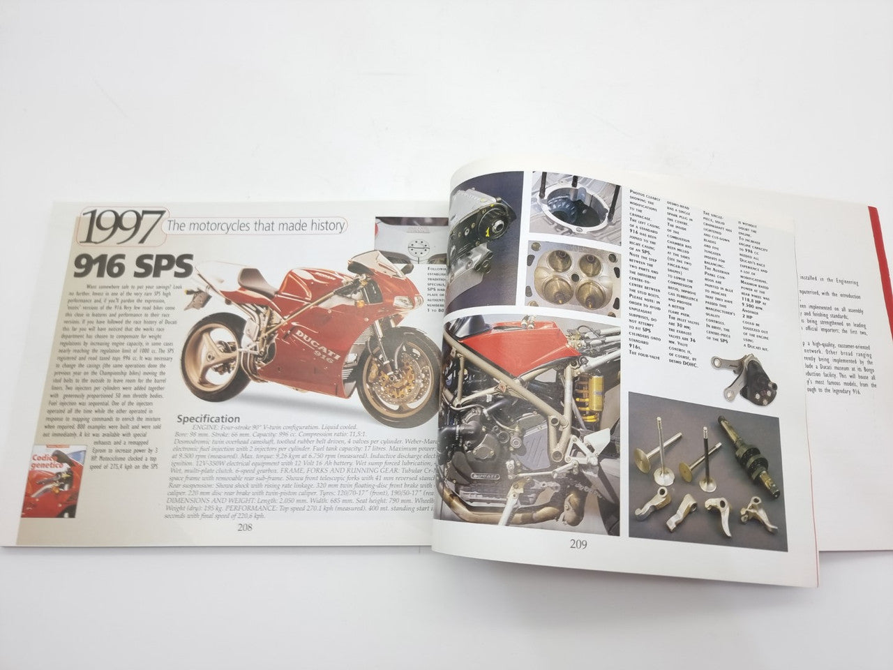 Open motorcycle history book spread with red 1997 916 bike image and engine parts
