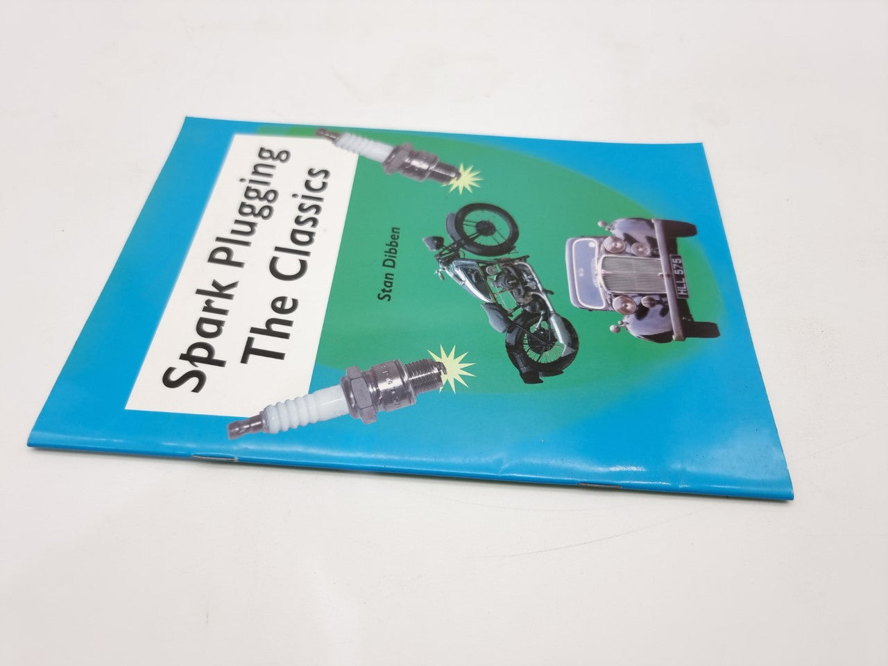 Paperback book cover with spark plug illustrations and title block, blue cover, angled