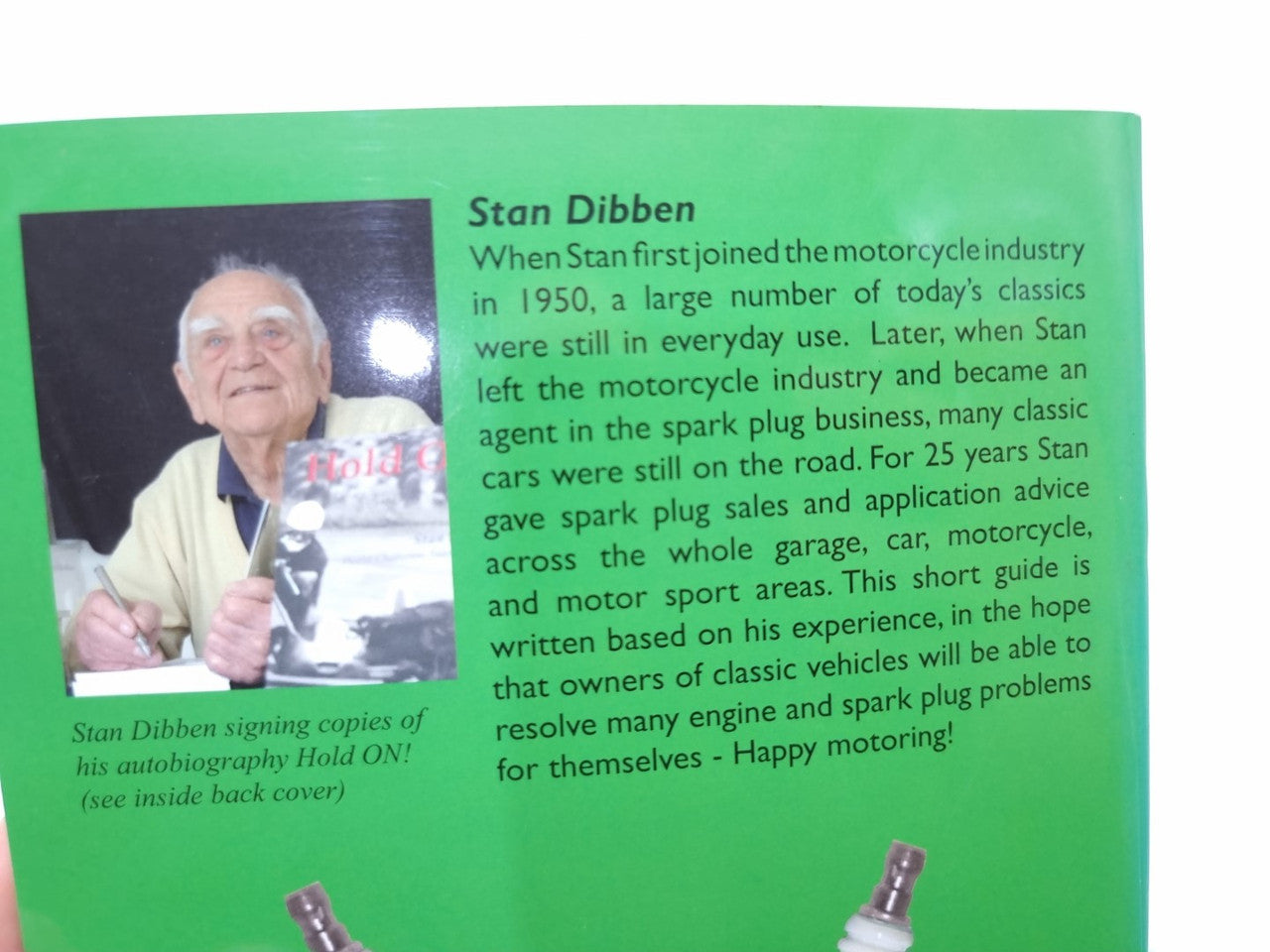 Paperback book biography page with portrait photo and two spark plugs on green