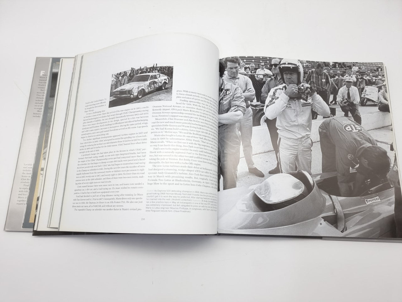 Open motorsport book showing large race car photo and crowd scene on the spread.