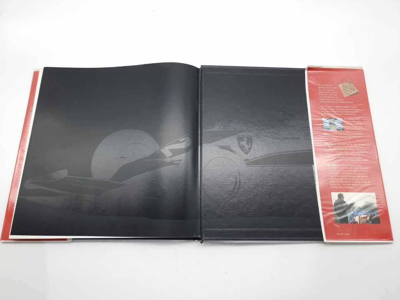 Open hardcover book with a dark graphic layout and faint steering wheel image on both pages