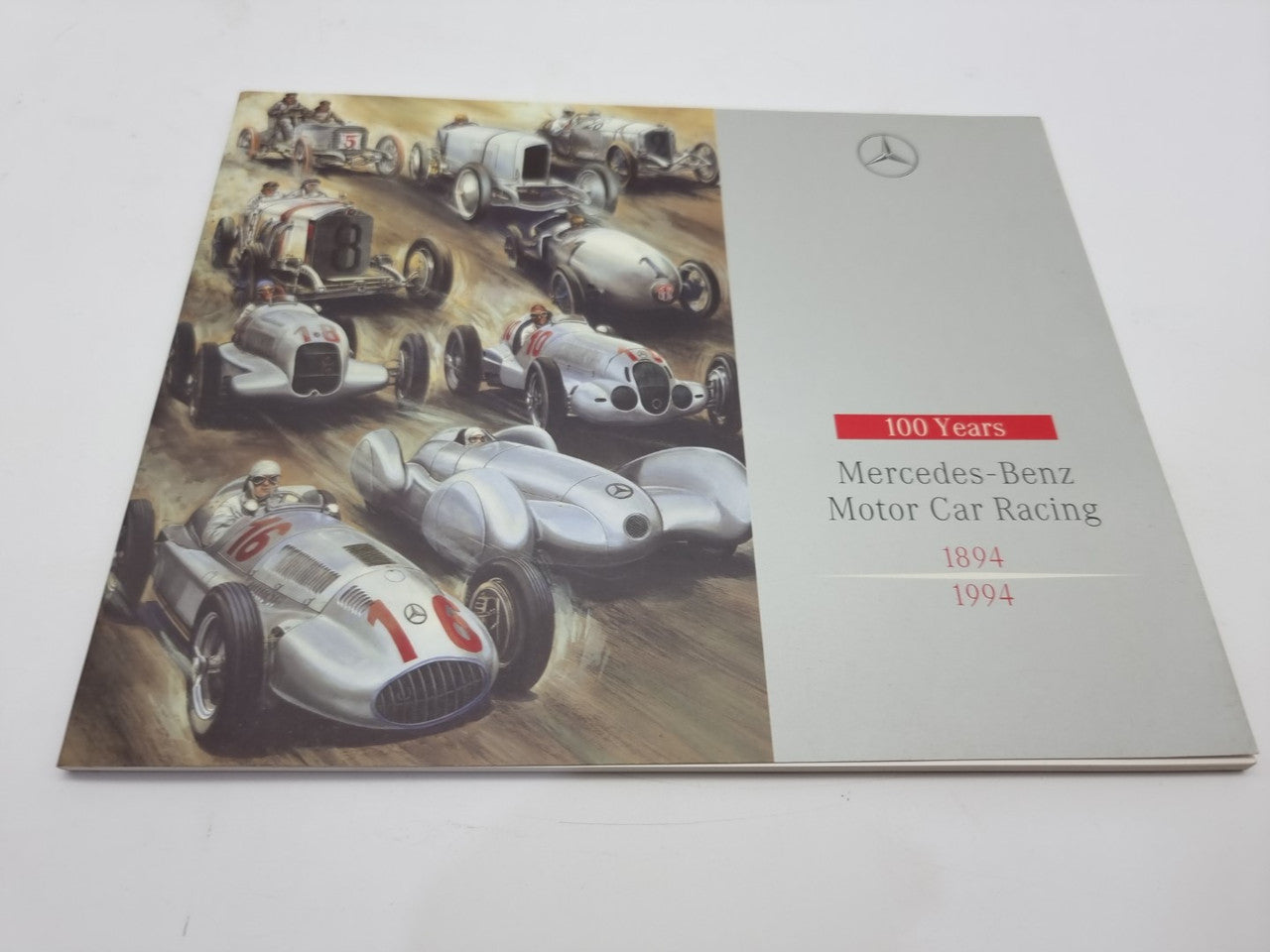 Motorsport history book cover with racing cars artwork and title text on white panel.