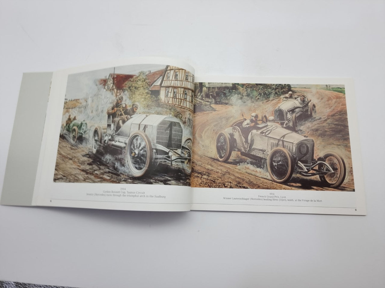 Motorsport history book with open pages showing vintage race cars on scenic track scenes.