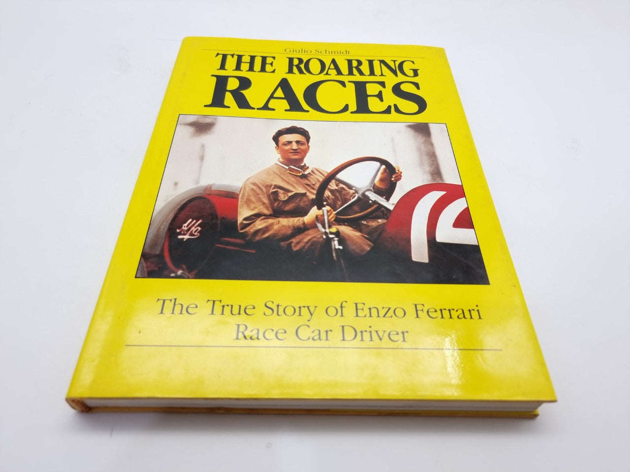 Yellow hardcover book cover with “THE ROARING RACES” title and a driver holding a steering wheel