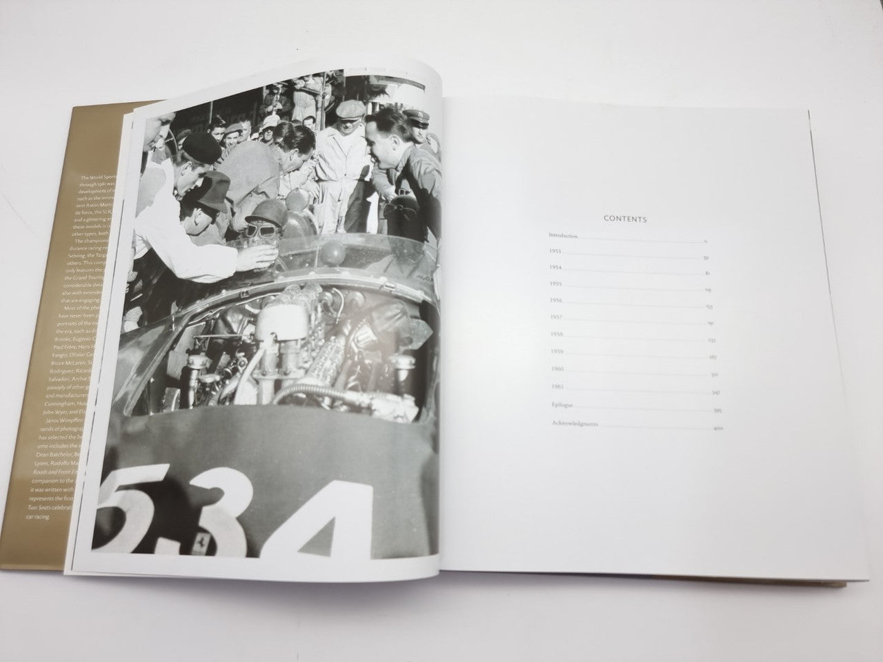 Opened hardcover book page with black-and-white photo of car engine and crew