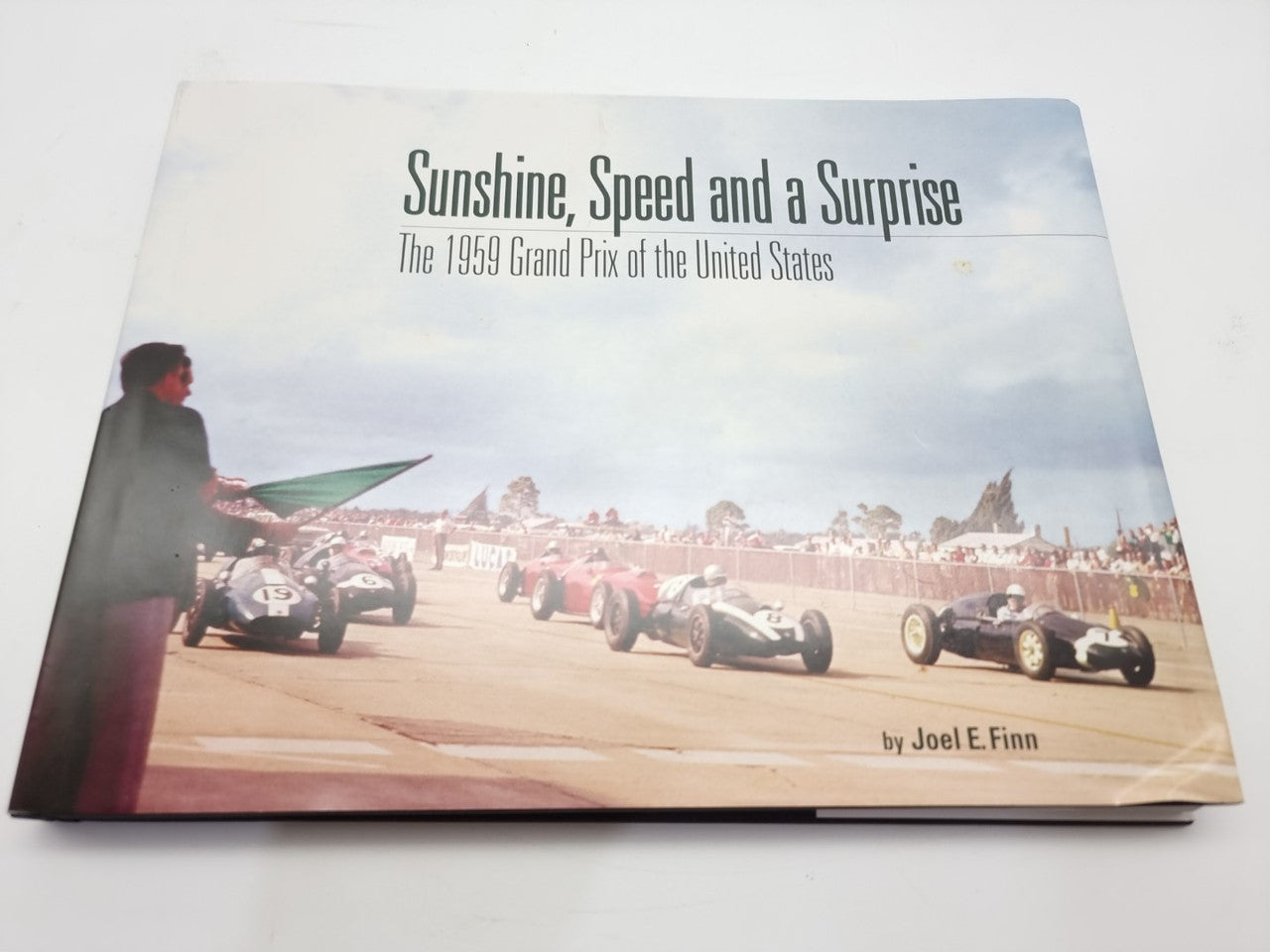 Vintage racing book cover with title text, race cars lined up, and author credit
