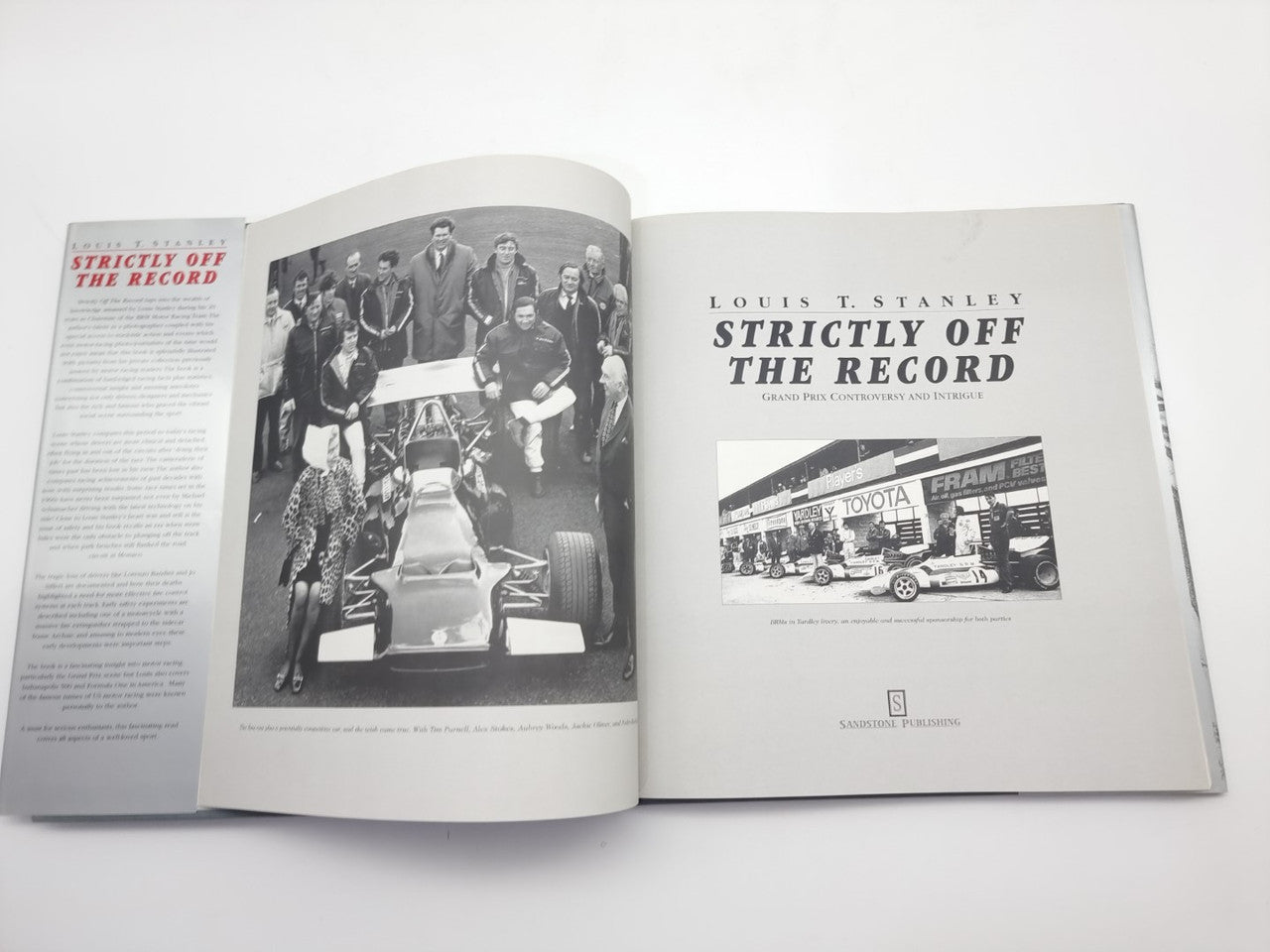 Racing history book open showing multiple photo pages and a car workshop image