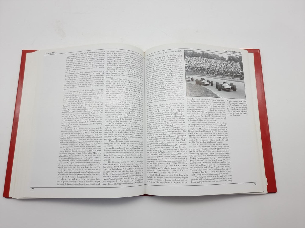 Open hardcover book with red cover, densely printed pages with small race-photo inset
