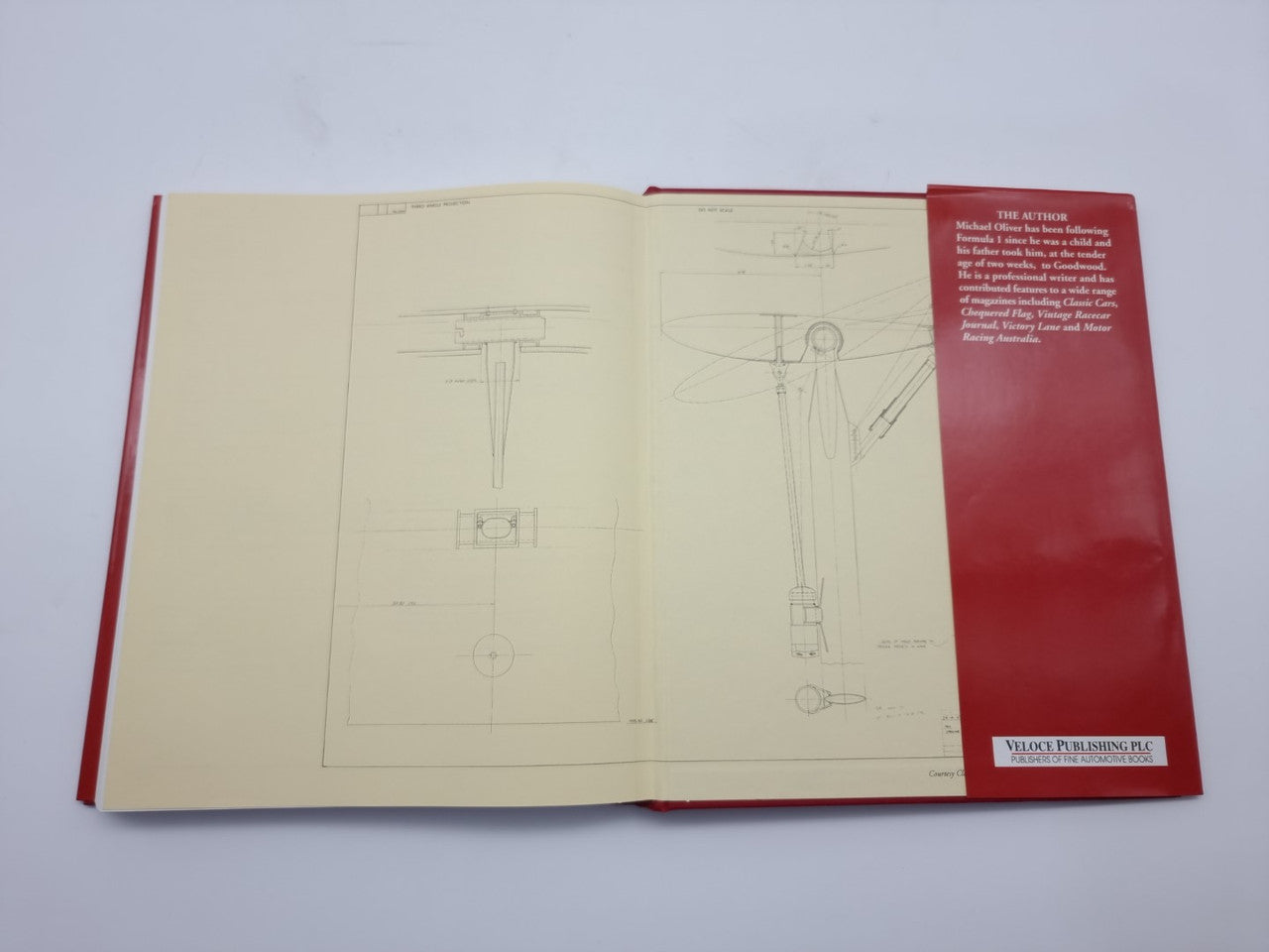 Open hardcover book with red cover, blueprint-style diagrams and labeled technical drawings