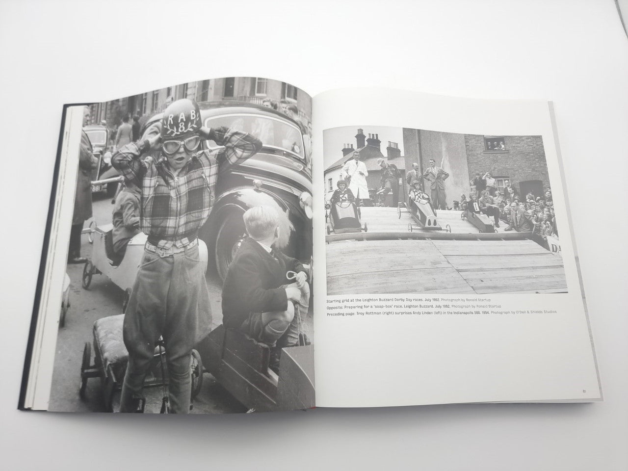 Open motor racing photo book with two black-and-white race scene photographs