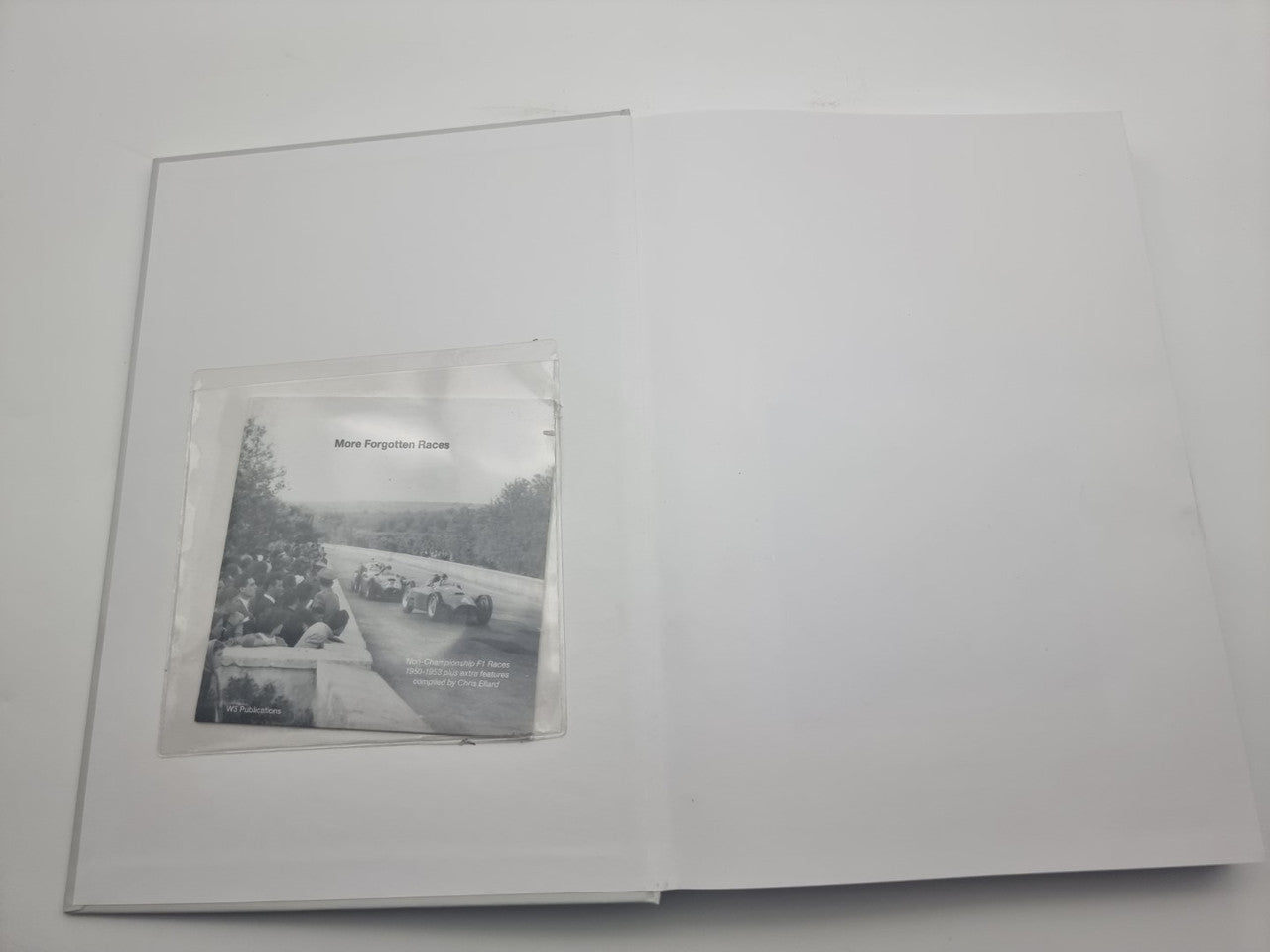 Open motorsport history book with a small race photo insert on the page
