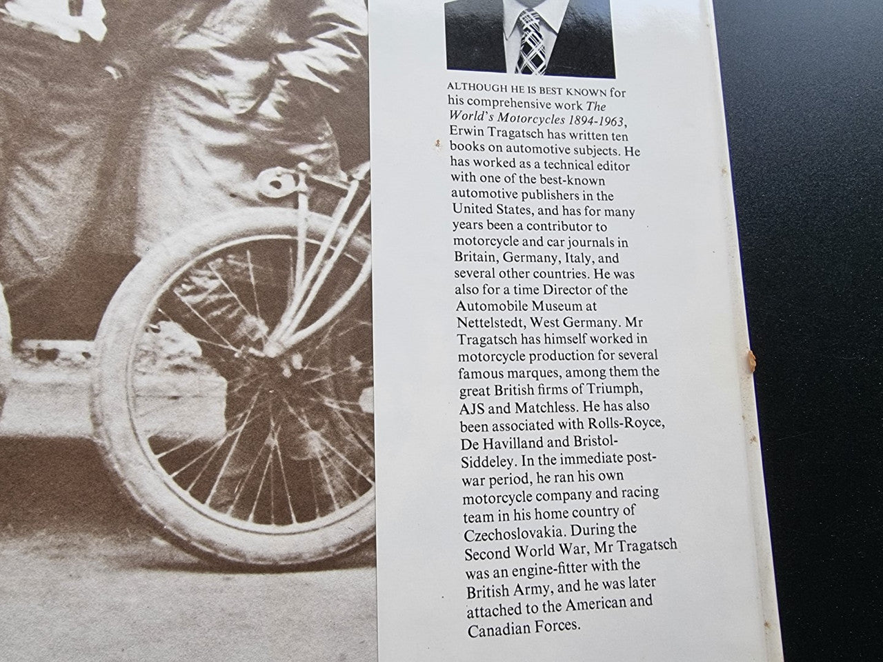 Motorcycle encyclopedia book page close-up with text and partial wheel photo at edge