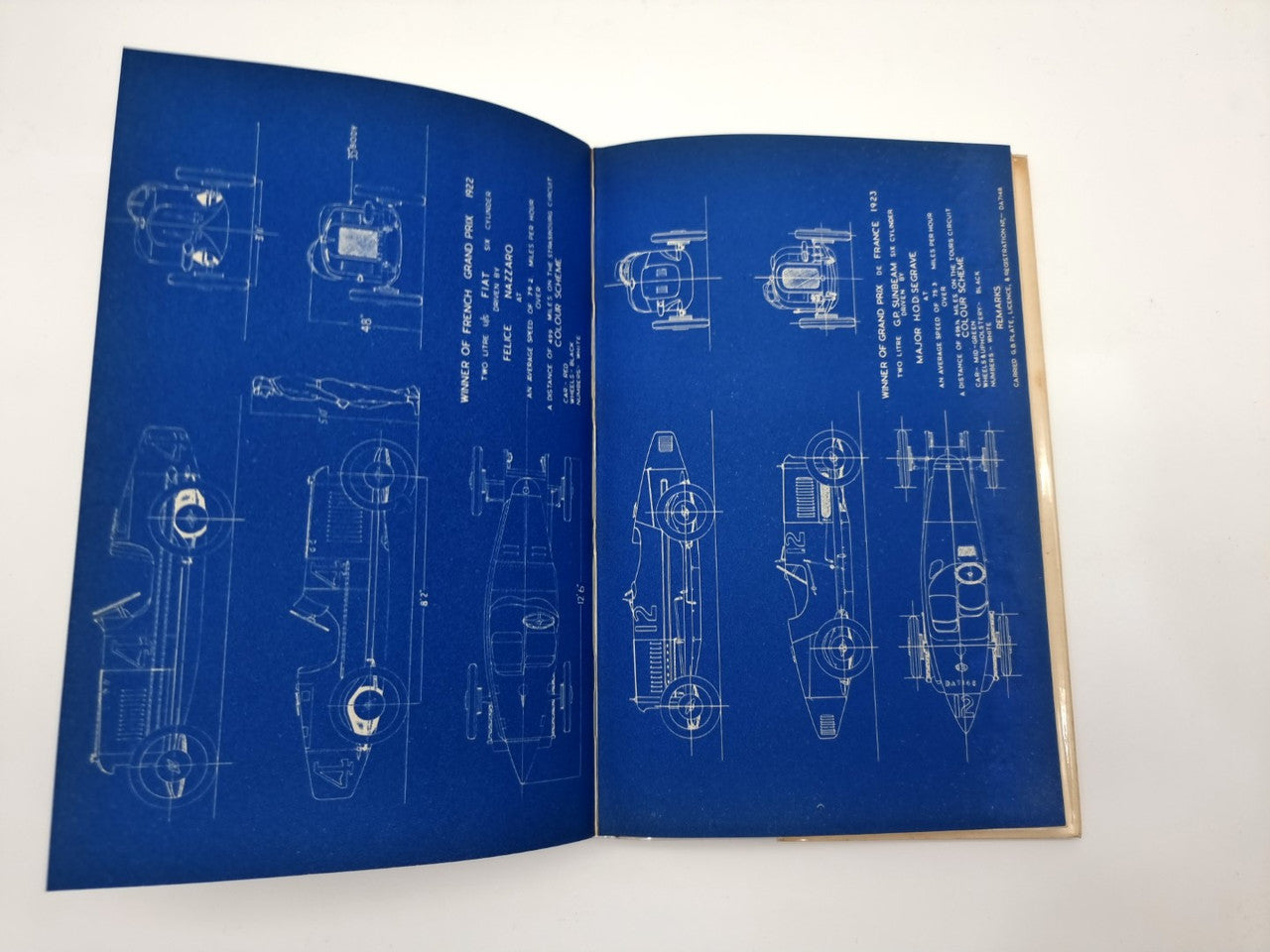 Vintage motorsport book open, blue pages with labeled technical schematics