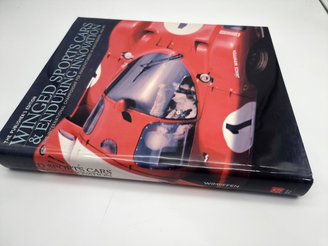 Hardcover book with red and dark sports car cover artwork, angled view