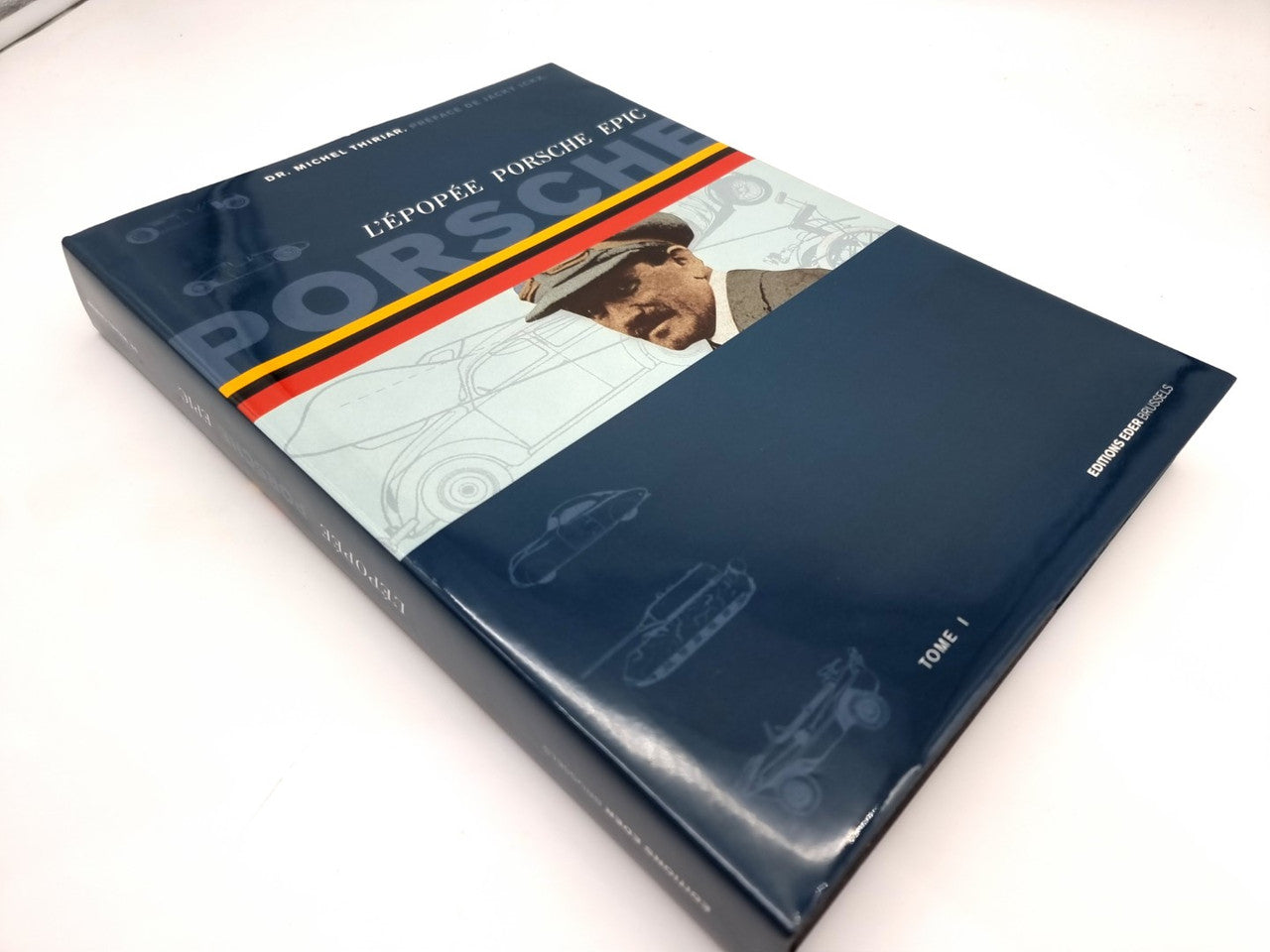 Closed blue hardcover book with orange stripe and illustrated Porsche scene on cover