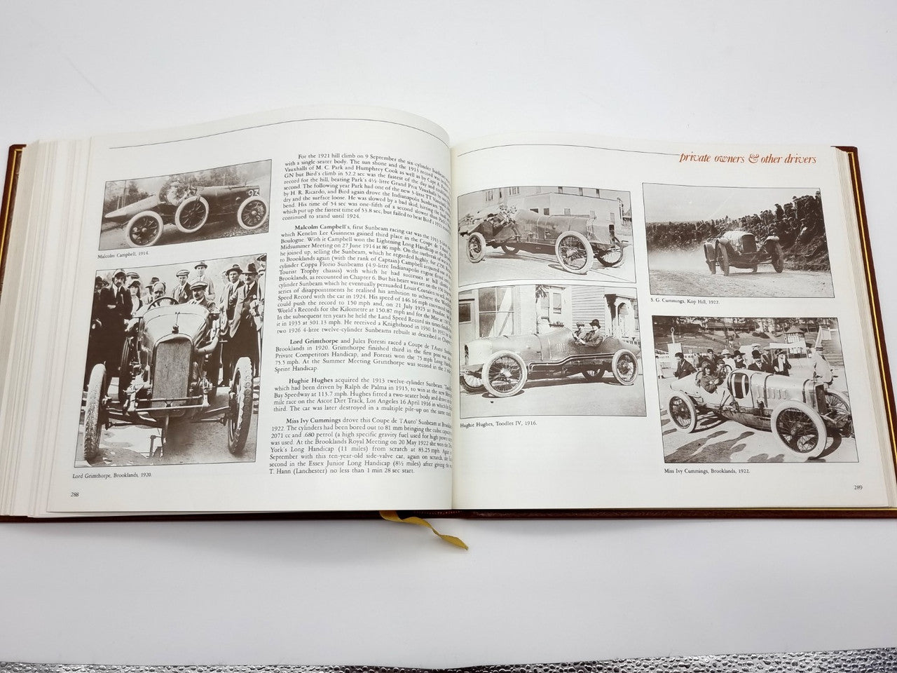 Open brown leatherbound book with black-and-white car photos and dense text