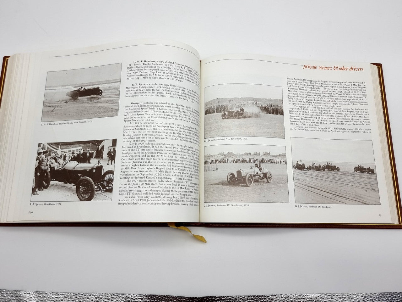 Open brown leatherbound book with multiple black-and-white car photos and captions