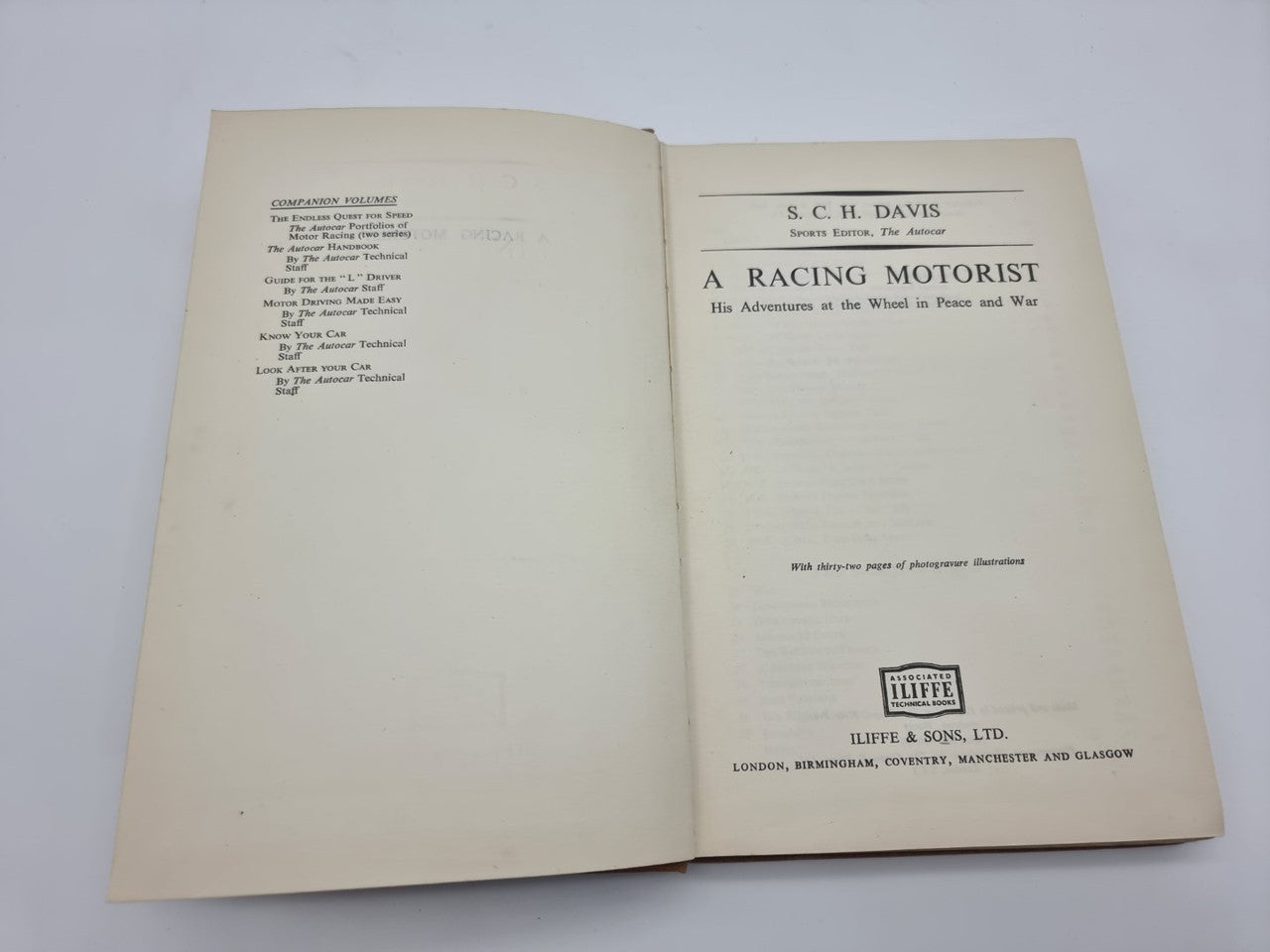 Hardcover book open; front title page shows 'A Racing Motorist' and publisher text