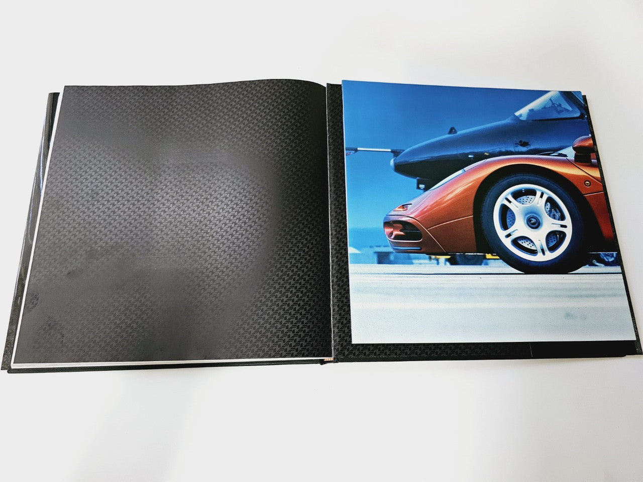 Open hardcover book spread with textured black pages and a color car photo