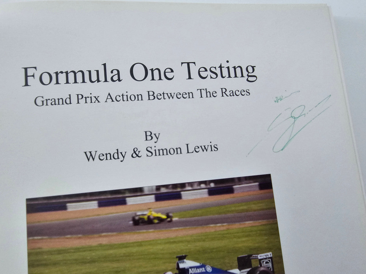 Open book page with title text and race photo, plus handwritten signature mark