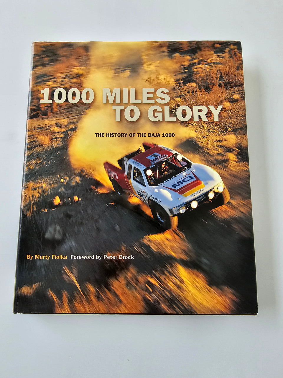 Book cover with title 1000 Miles to Glory and race car on desert road
