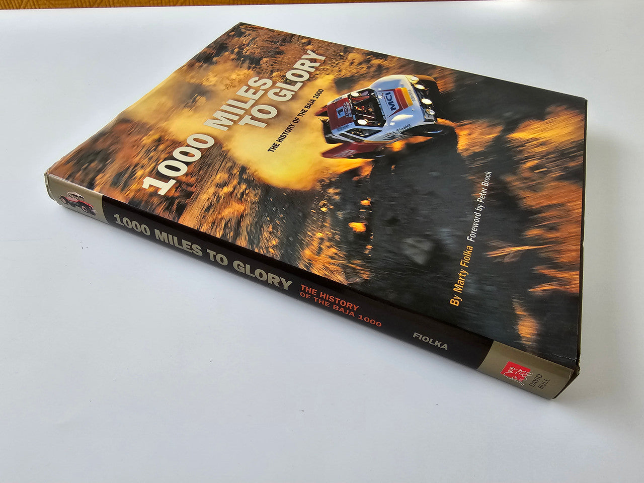 Hardcover book with Baja 1000 cover artwork, racing vehicle on dusty terrain.
