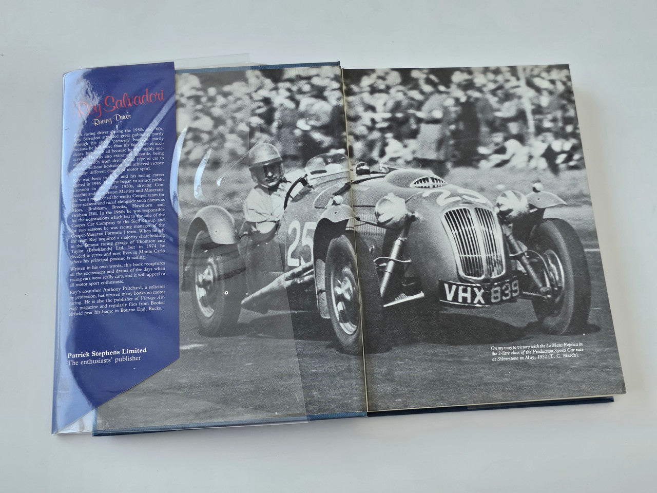 Open racing driver book spread with grayscale car photo and blue text panel on left.