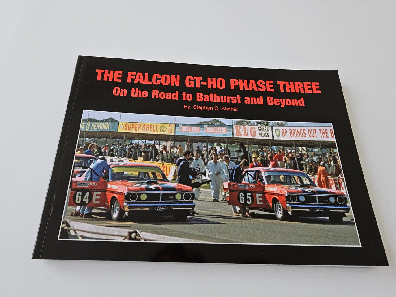 Limited edition automotive book cover with red title text and photo of two orange race cars
