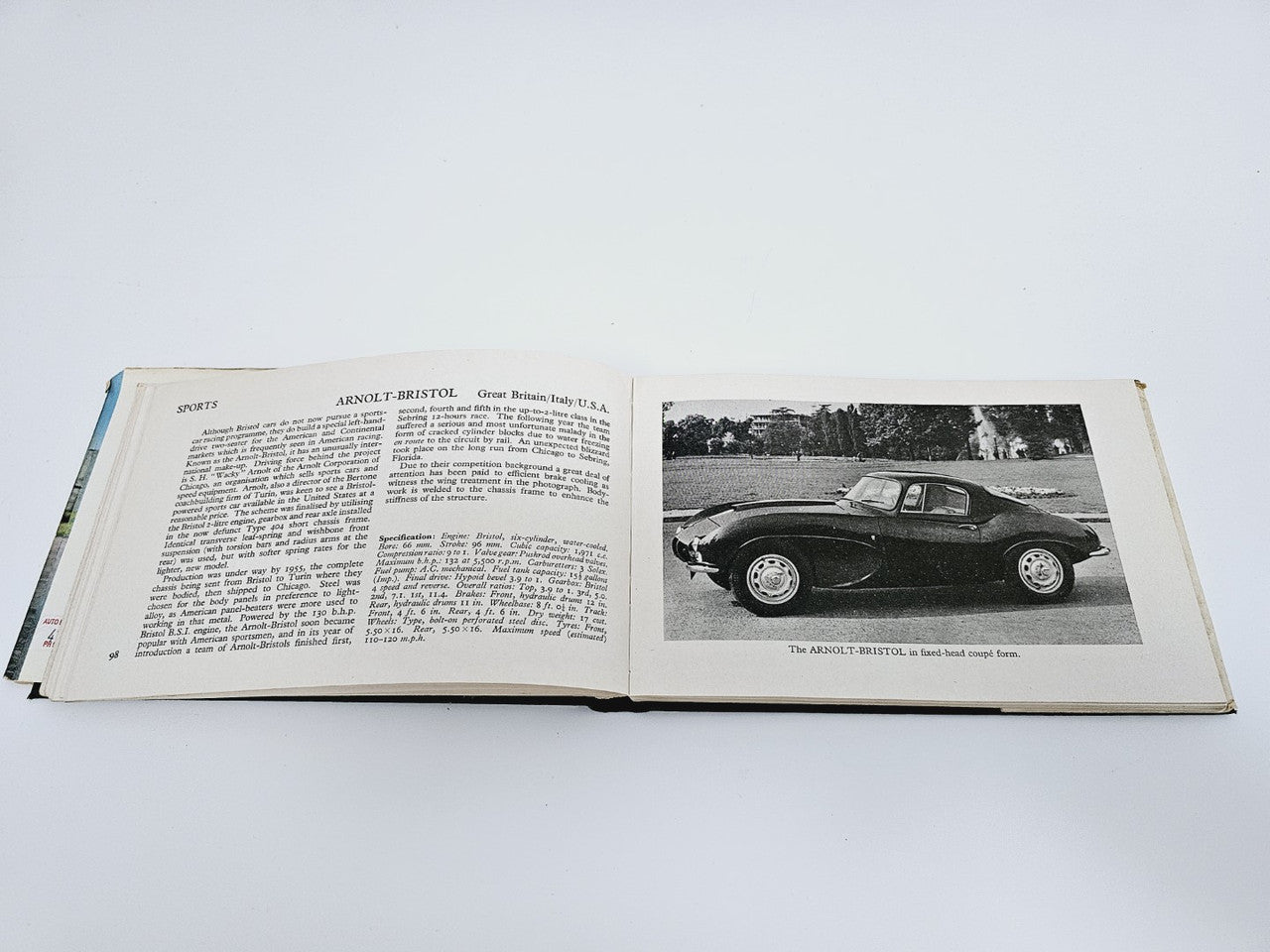 Open book with vehicle history text on the left and a dark race car photo on the right