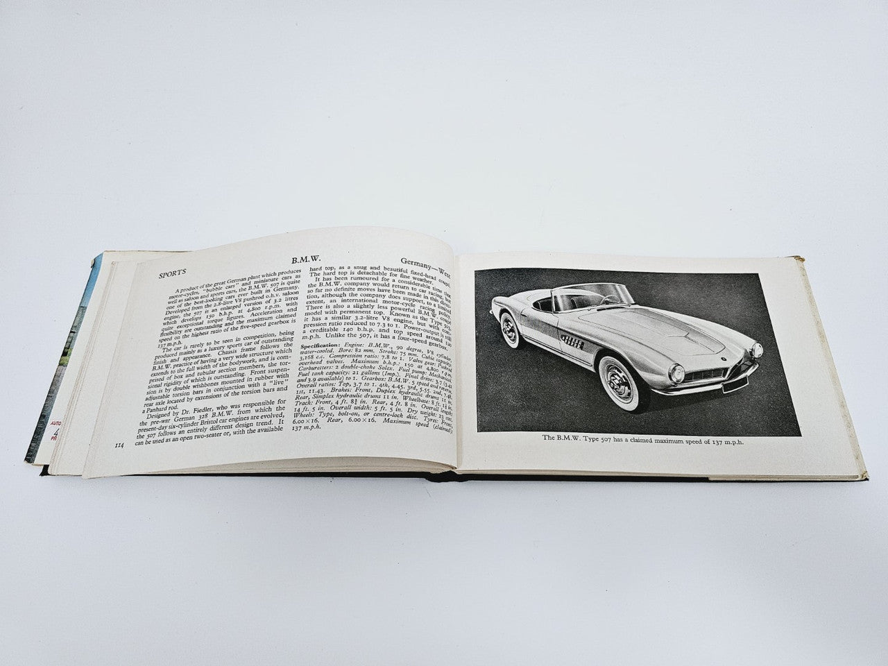 Open vintage racing cars book with text column and black-and-white sports car photo