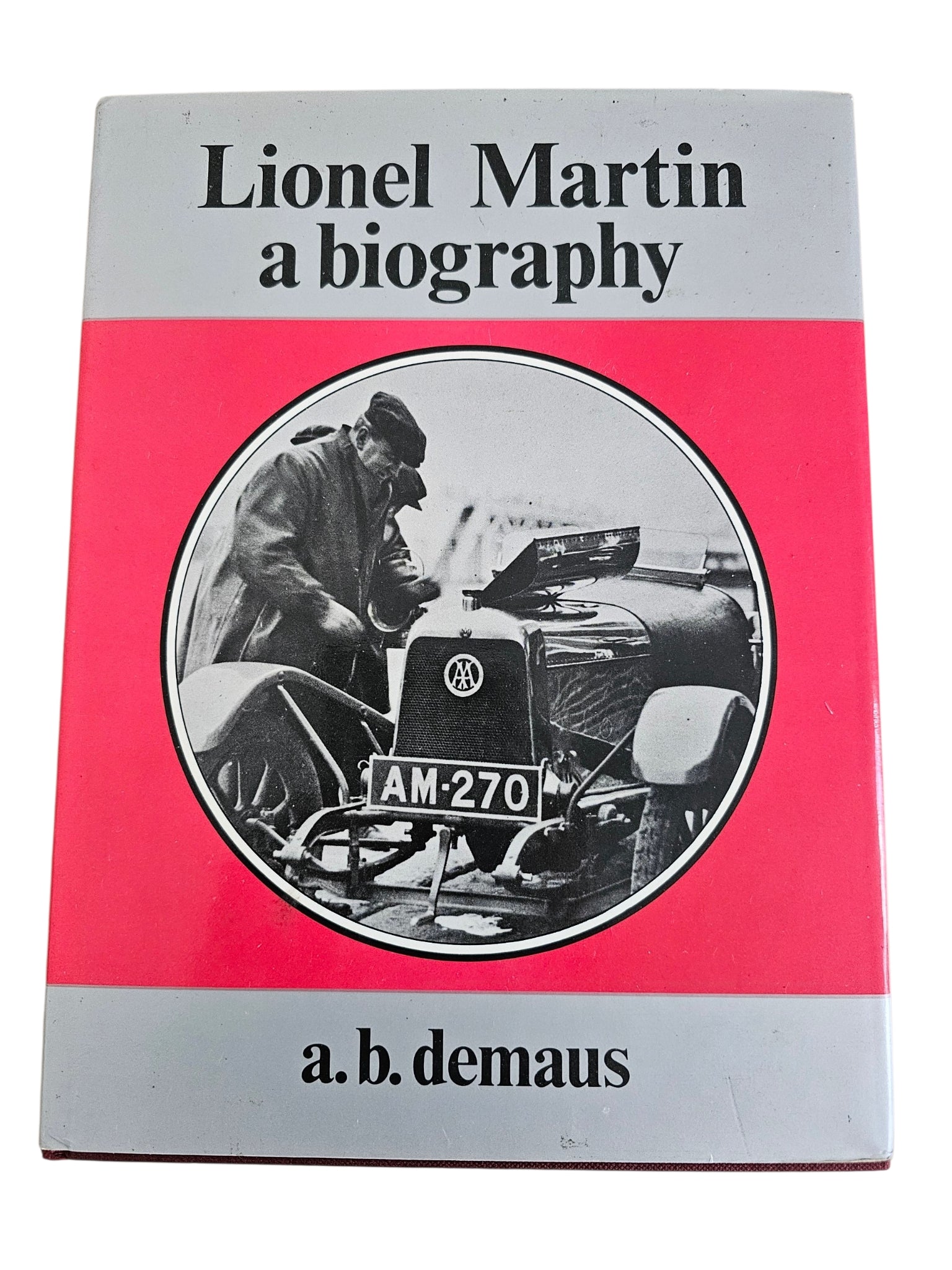 Hardcover biography book cover with gray top, red middle, and round car photo