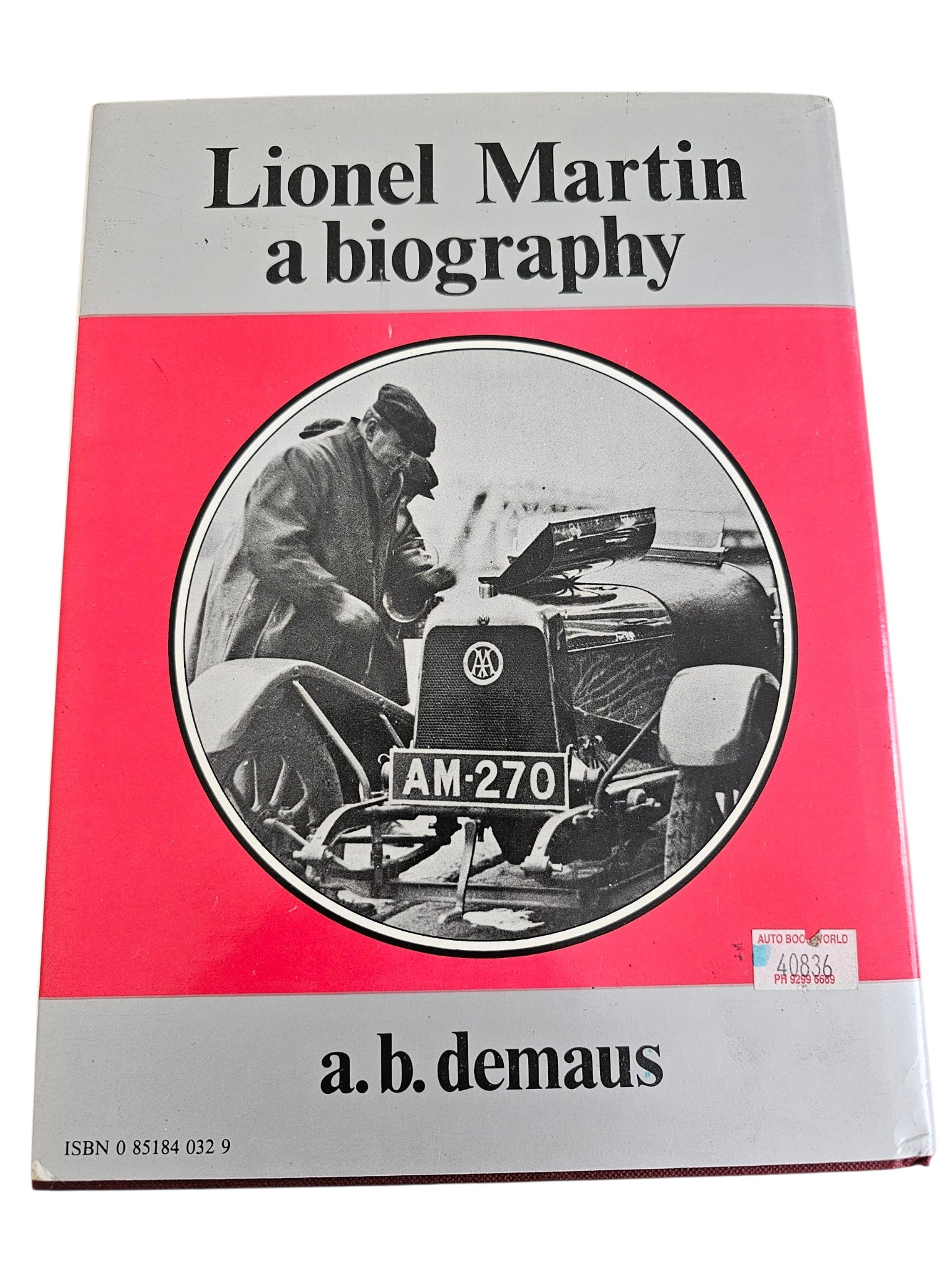 Hardcover biography book cover with red panel, round car photo, and barcode sticker