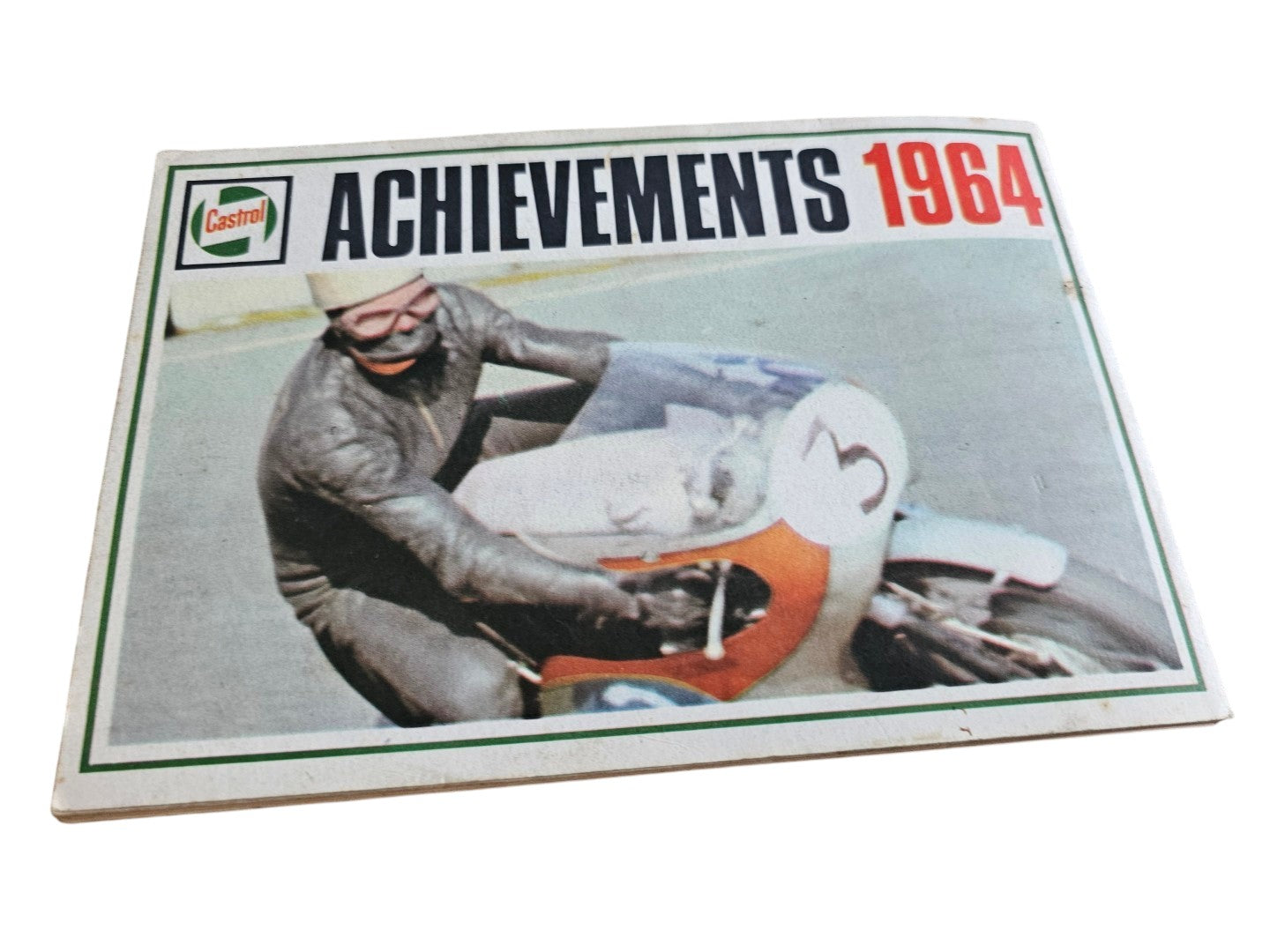 Vintage booklet cover close-up of driver and orange race car under the “Achievements 1964” header