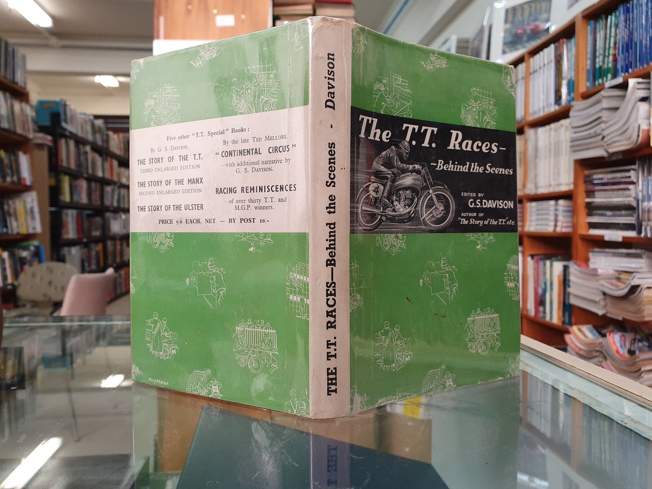 Green book with "The T.T. Races—Behind the Scenes" on display among shelves