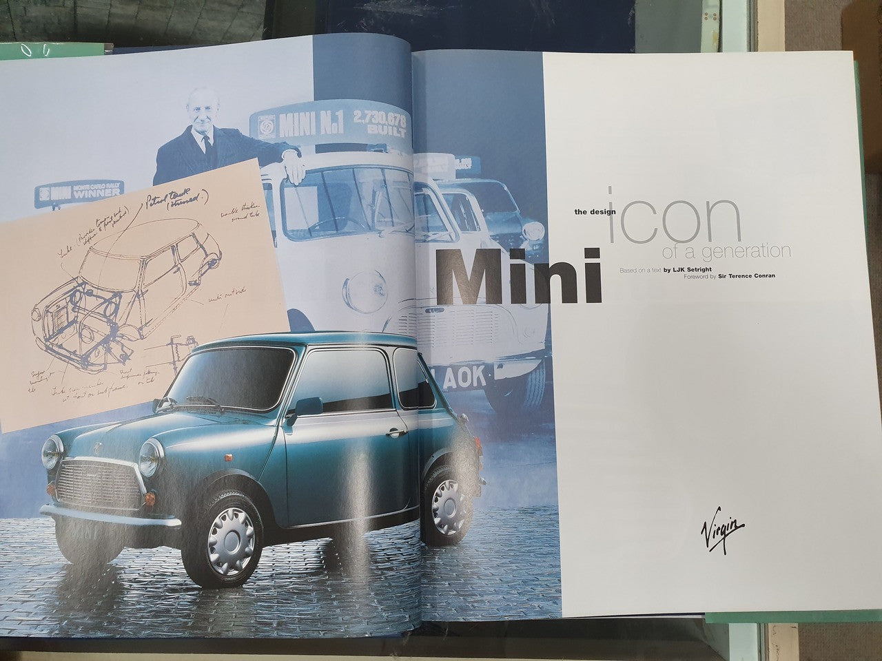 Hardcover photo book open to pages with a blue Mini car and vehicle sketches