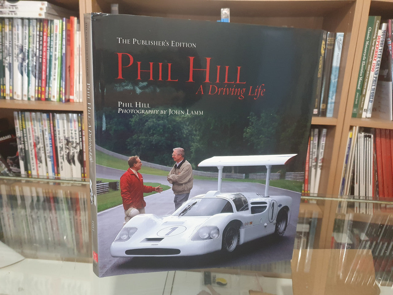 Hardcover book on shelf, dark green cover with red title and race car image