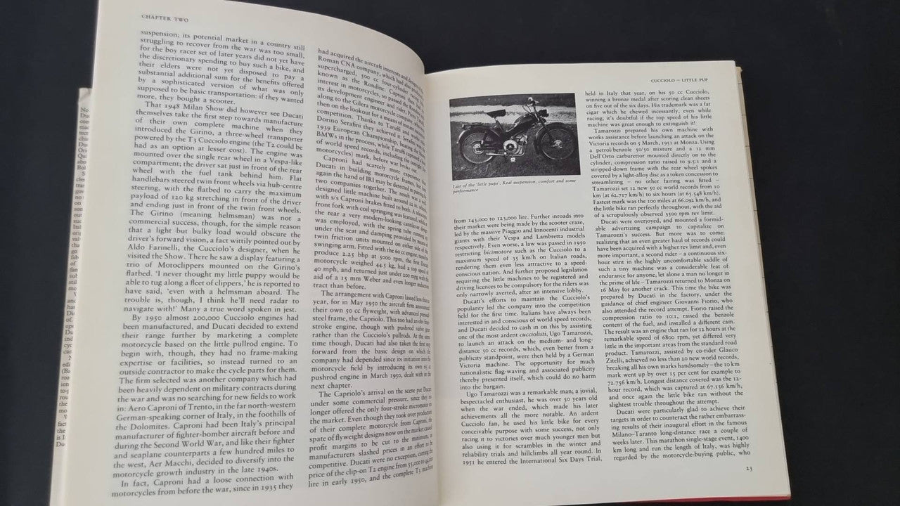 Open vintage book spread with dense text and small grayscale motorcycle engine photo
