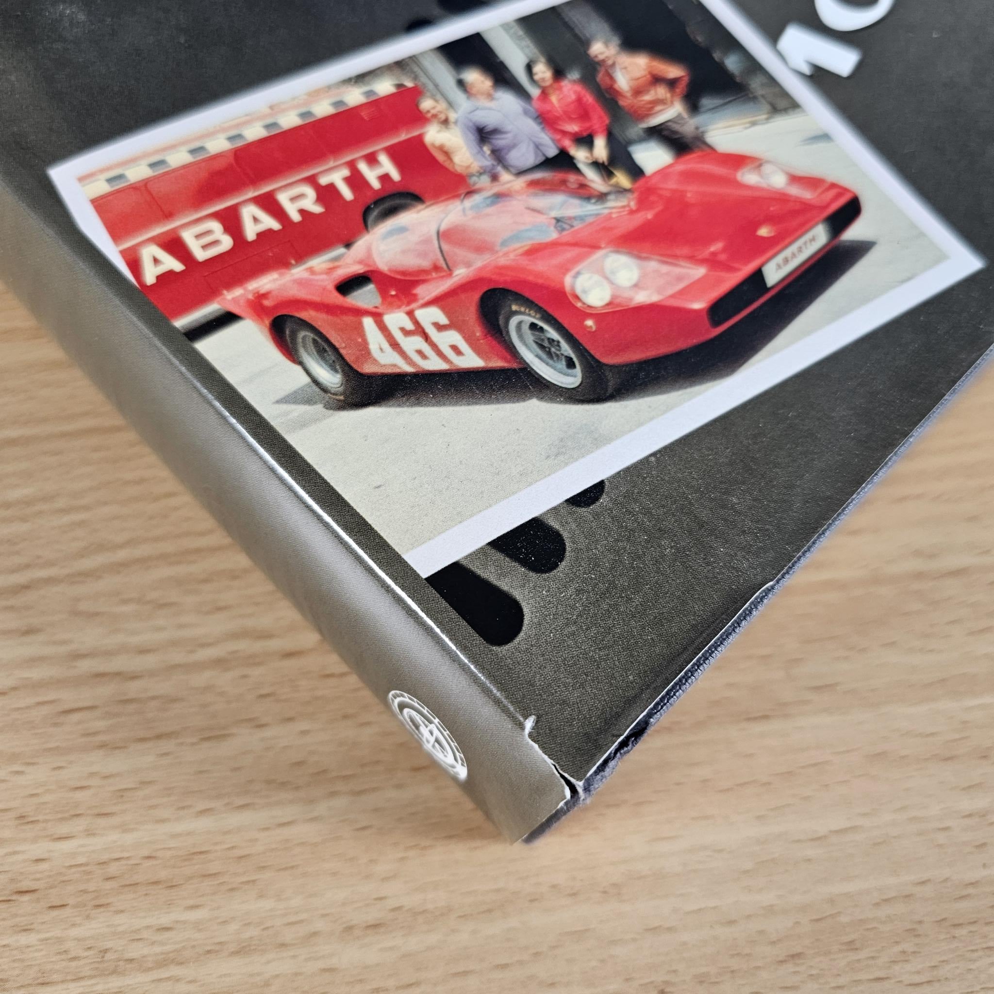 Hardcover car book cover corner with red sports car photo on a dark surface.