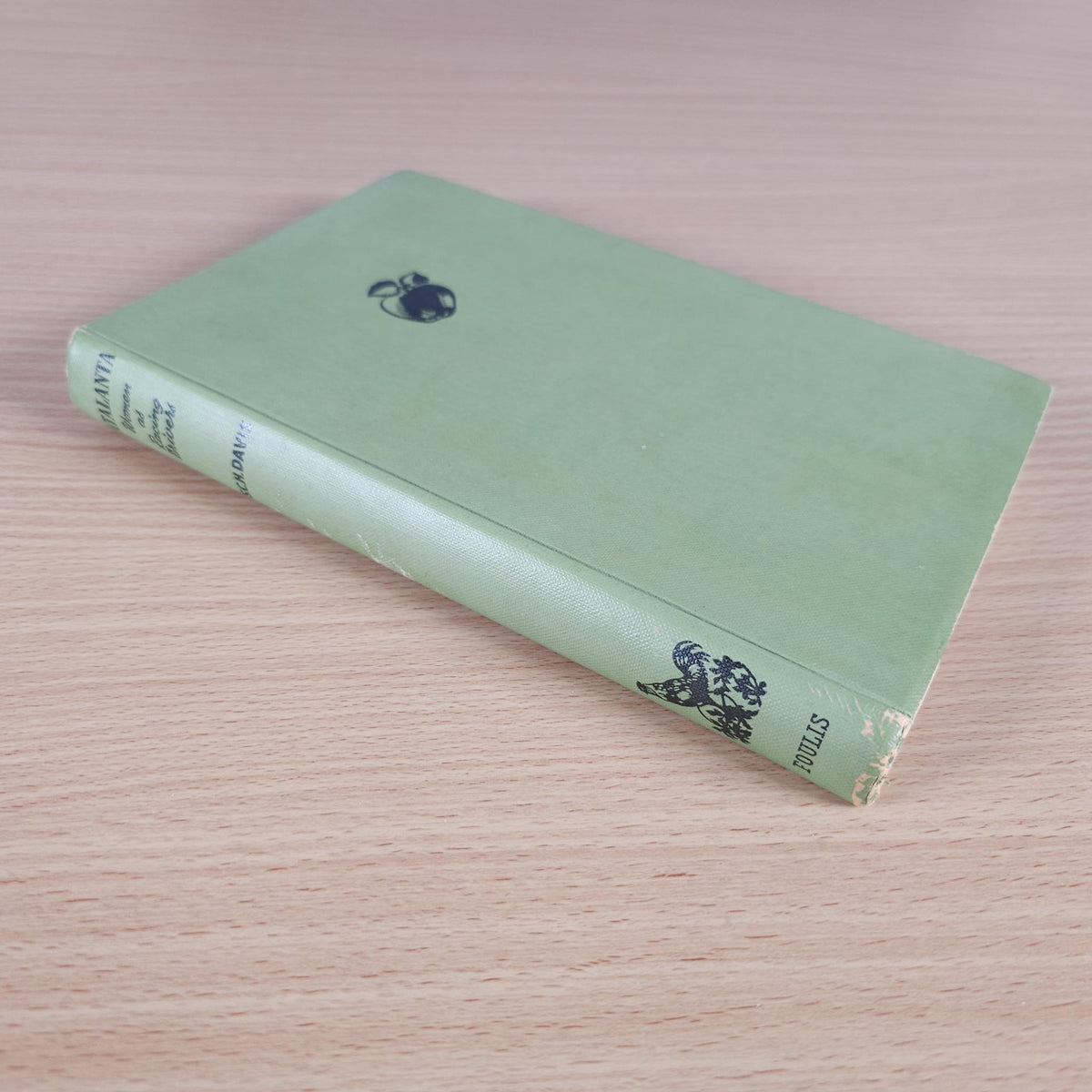 Green hardcover book lying on a wood surface, small icon on front cover.