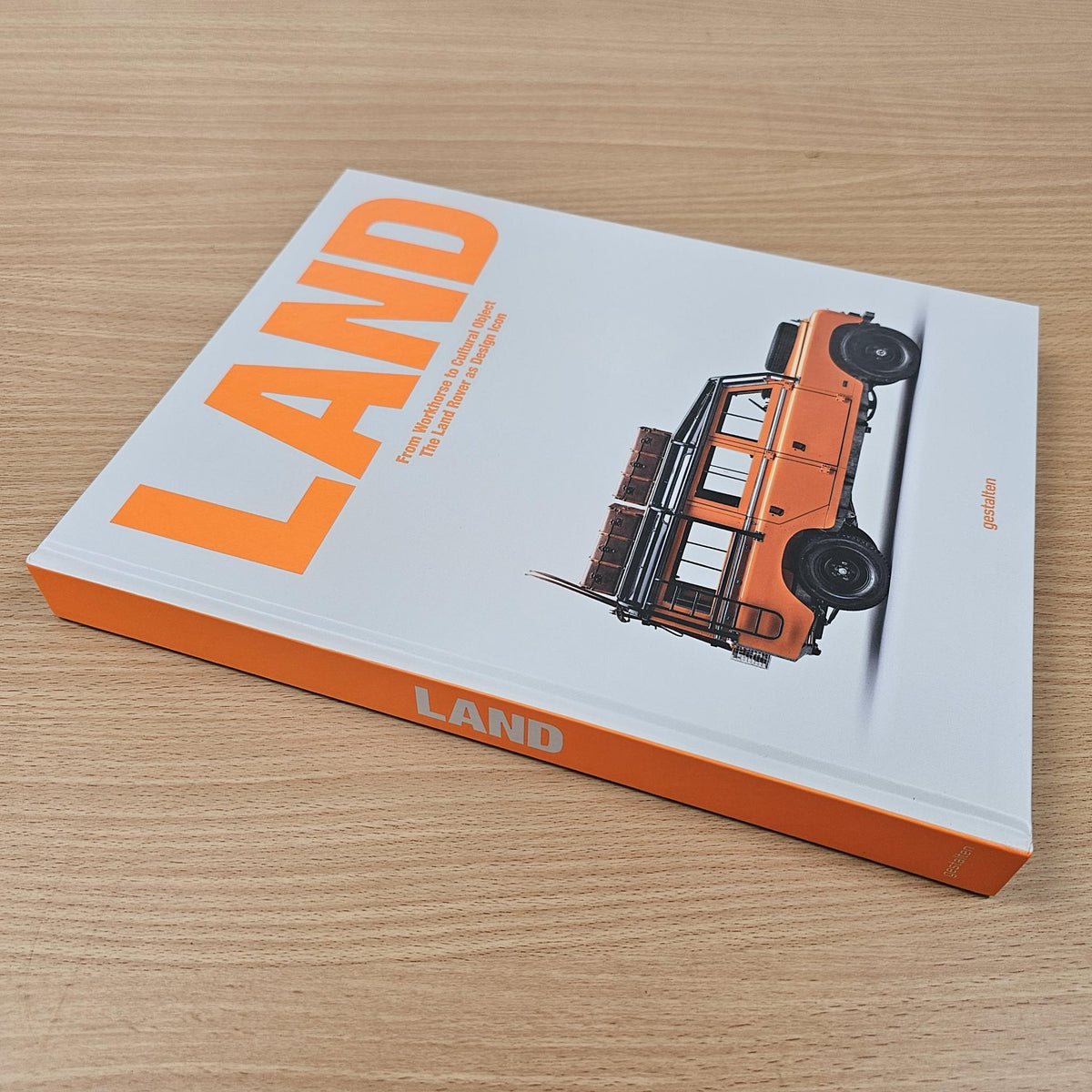 Land Rover hardcover book lying on wood with orange title and vehicle image