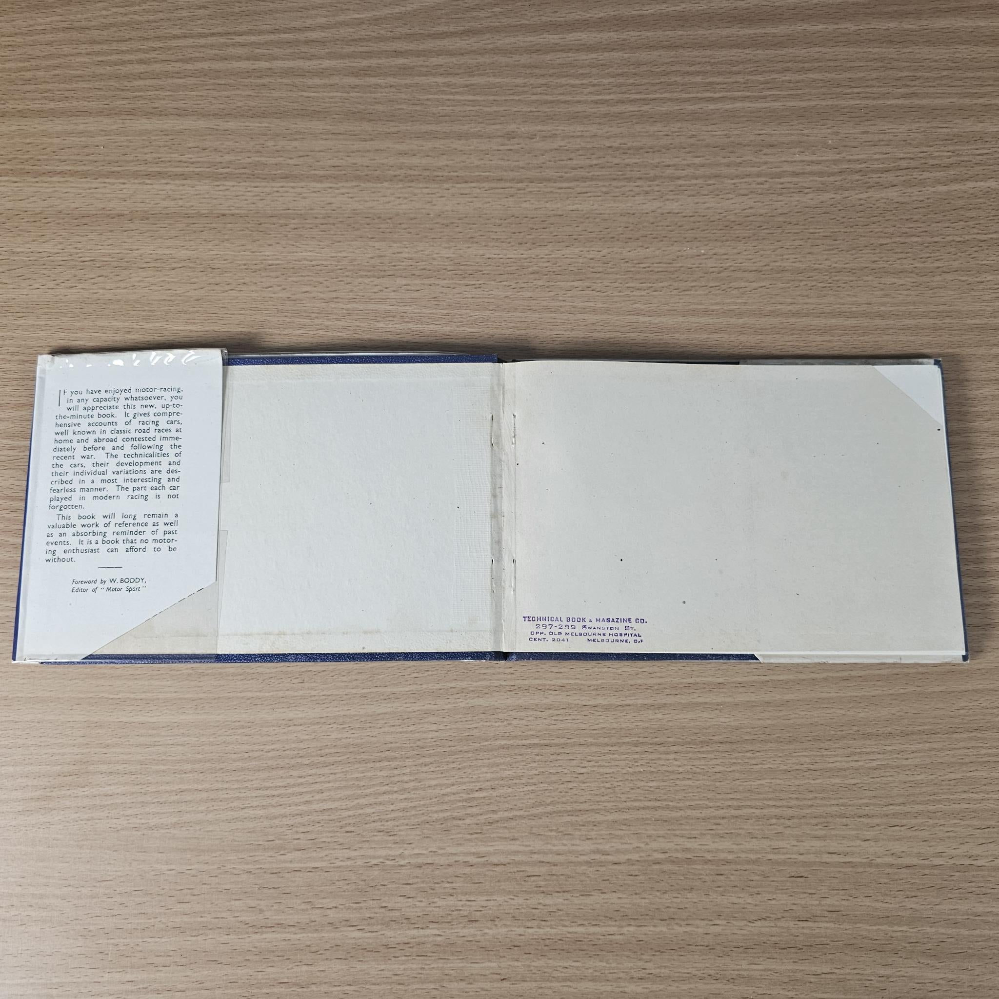 Vintage racing car review book open to blank white pages with a small note sheet