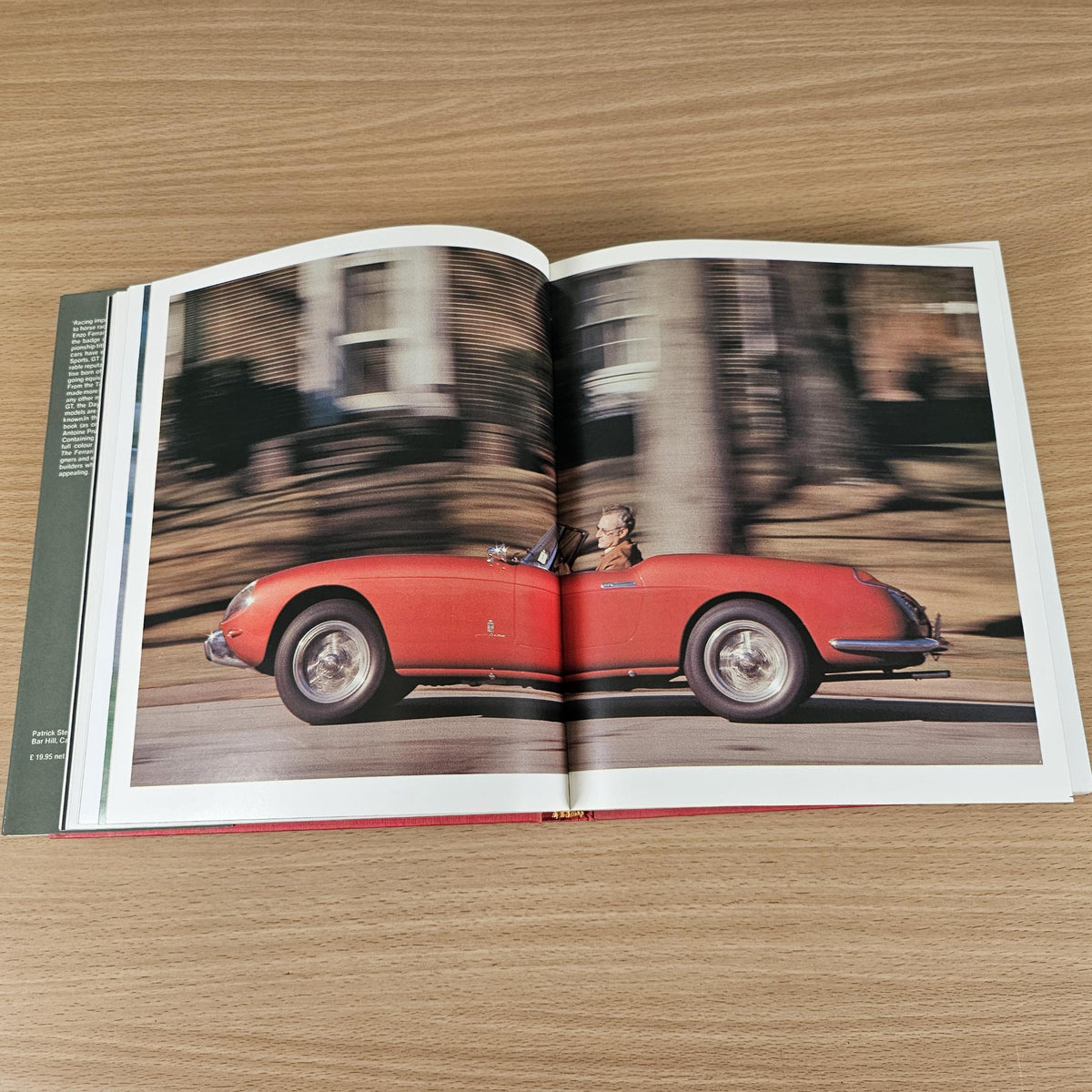 Open vintage sports car photo book with red road car image spread.